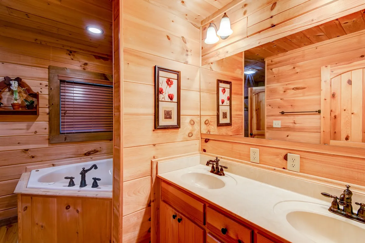 An elegant bathroom featuring double vanity sinks, a whirlpool tub, framed artwork, and wooden accents. The space is serene and welcoming, emphasizing relaxation and self-care.
