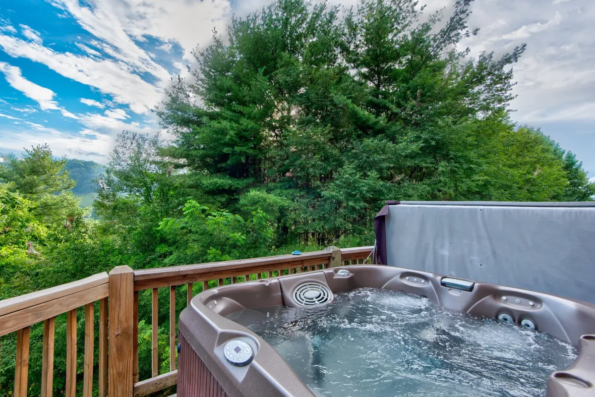 A serene covered deck with a bubbling hot tub surrounded by lush trees and a sweeping view of the distant landscape. The space invites relaxation and offers a direct connection to the outdoors, perfect for unwinding with loved ones.