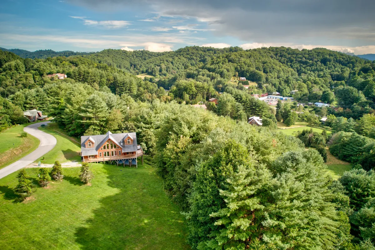 This image provides a wider contextual view of the property, highlighting the wooden house framed by tall trees and a winding mountain road. The setting invites thoughts of hiking, nature walks, and winter adventures, with the road hinting at the seasonal challenges and beauty of the High Country.
