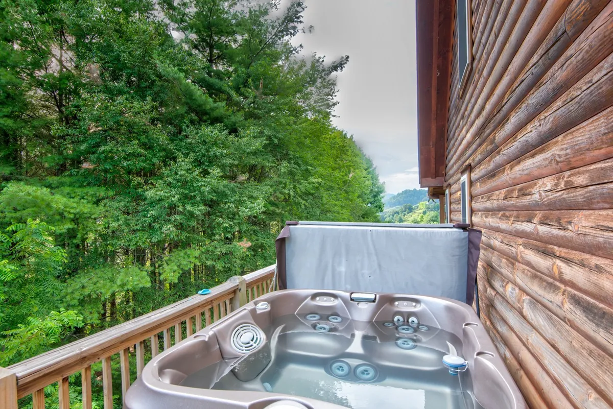 A serene exterior shot of a wooden deck with a bubbling hot tub, surrounded by lush greenery. The deck invites relaxation and offers space to soak under the stars, echoing the amenities highlighted in the text.