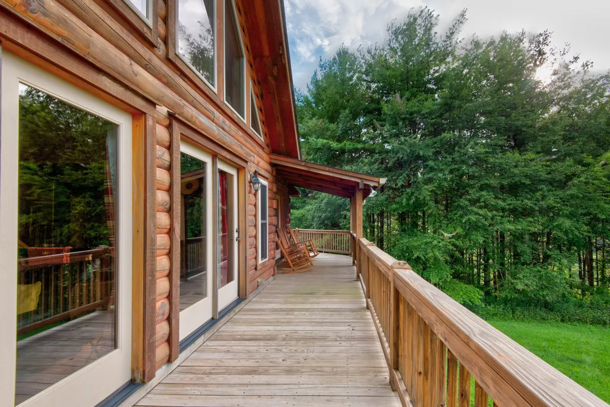 A tranquil wooden balcony with rocking chairs set against surrounding greenery, featuring large windows that connect the interior to sweeping outdoor views. The space invites moments of quiet reflection or socializing while enjoying the mountain air.