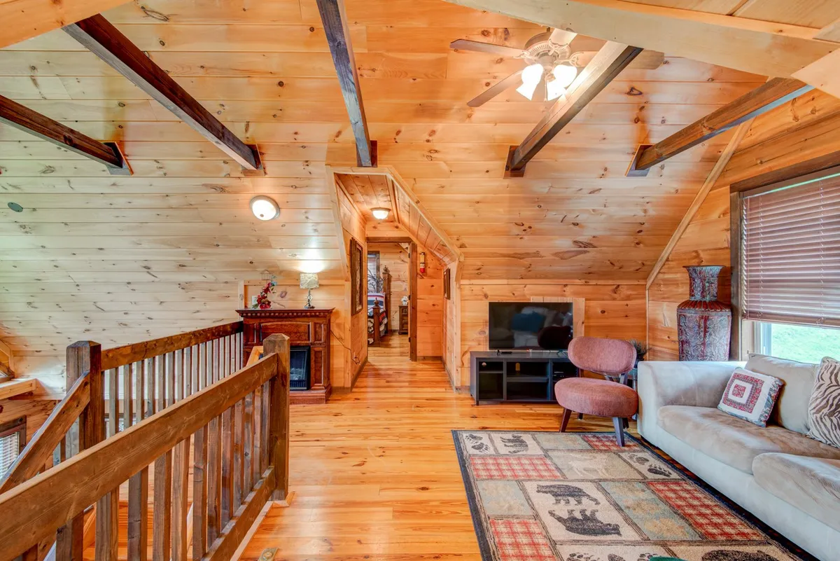 A comfortable living area with exposed wooden beams, a plush sofa, a textured rug, and a window inviting in natural light. The inviting space is perfect for relaxing, socializing, or curling up after a day outdoors, representing both cozy winter evenings and breezy summer afternoons.