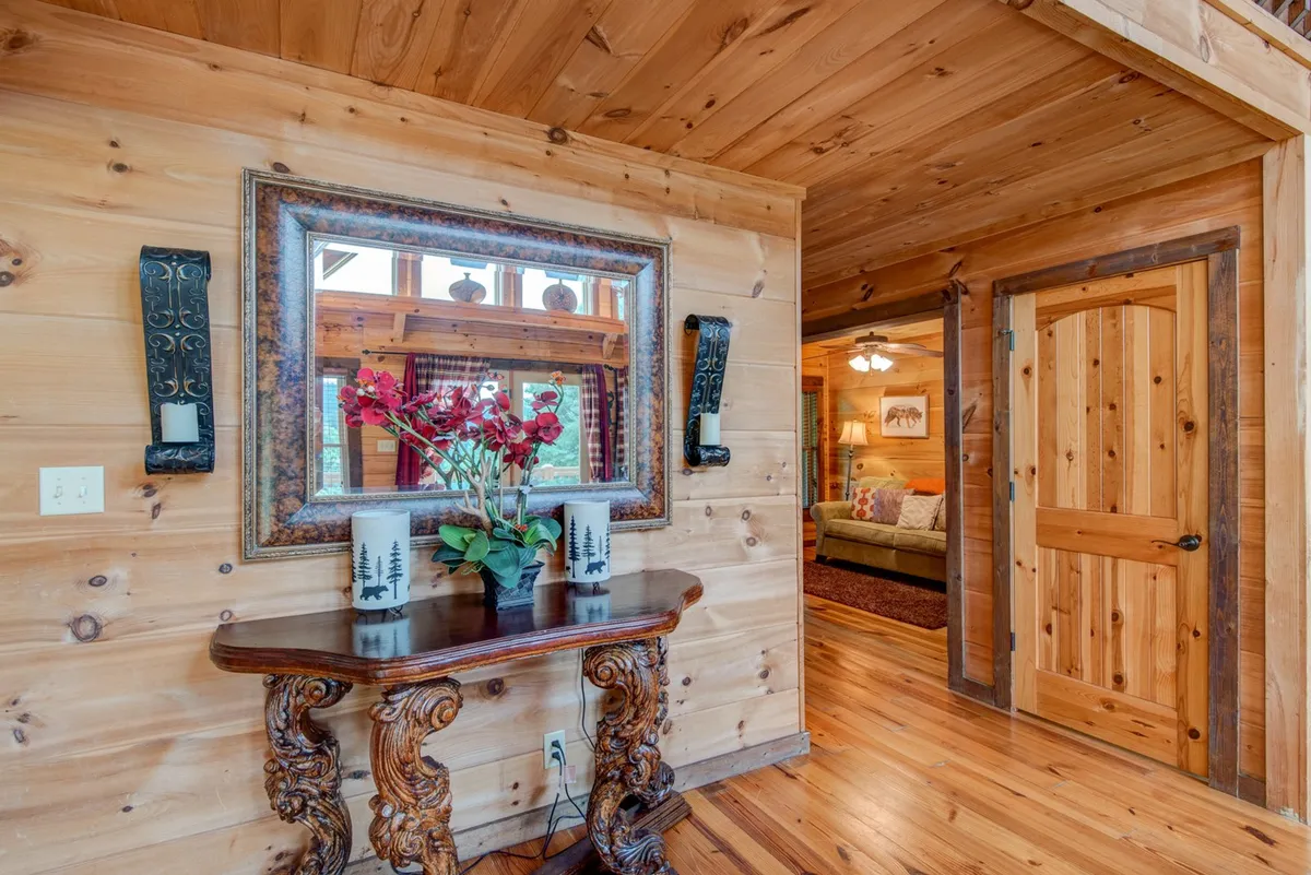 A welcoming entryway featuring an ornate wooden table topped with a flower arrangement, a mirror reflecting the warm light, and doorways leading further into the home. The decor suggests warmth and hospitality, providing a transitional space from the outdoors.