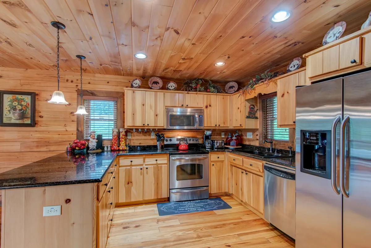 A modern kitchen featuring granite countertops, stainless steel appliances, warm wooden cabinetry, and inviting hanging light fixtures. The layout encourages socializing and cooking together, evoking a sense of home and hospitality.